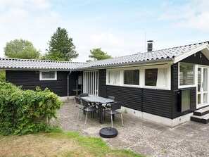 Une maison en bois peinte en noir, avec un toit recouvert de tuiles, une terrasse avec une table et des chaises, et un petit jardin.