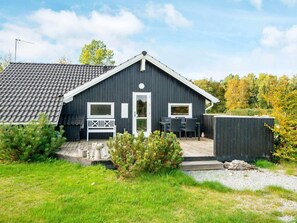 Ein zweistöckiges Haus mit dunkler Fassade, einer Veranda mit einer Bank und einer kleinen Terrassenfläche.