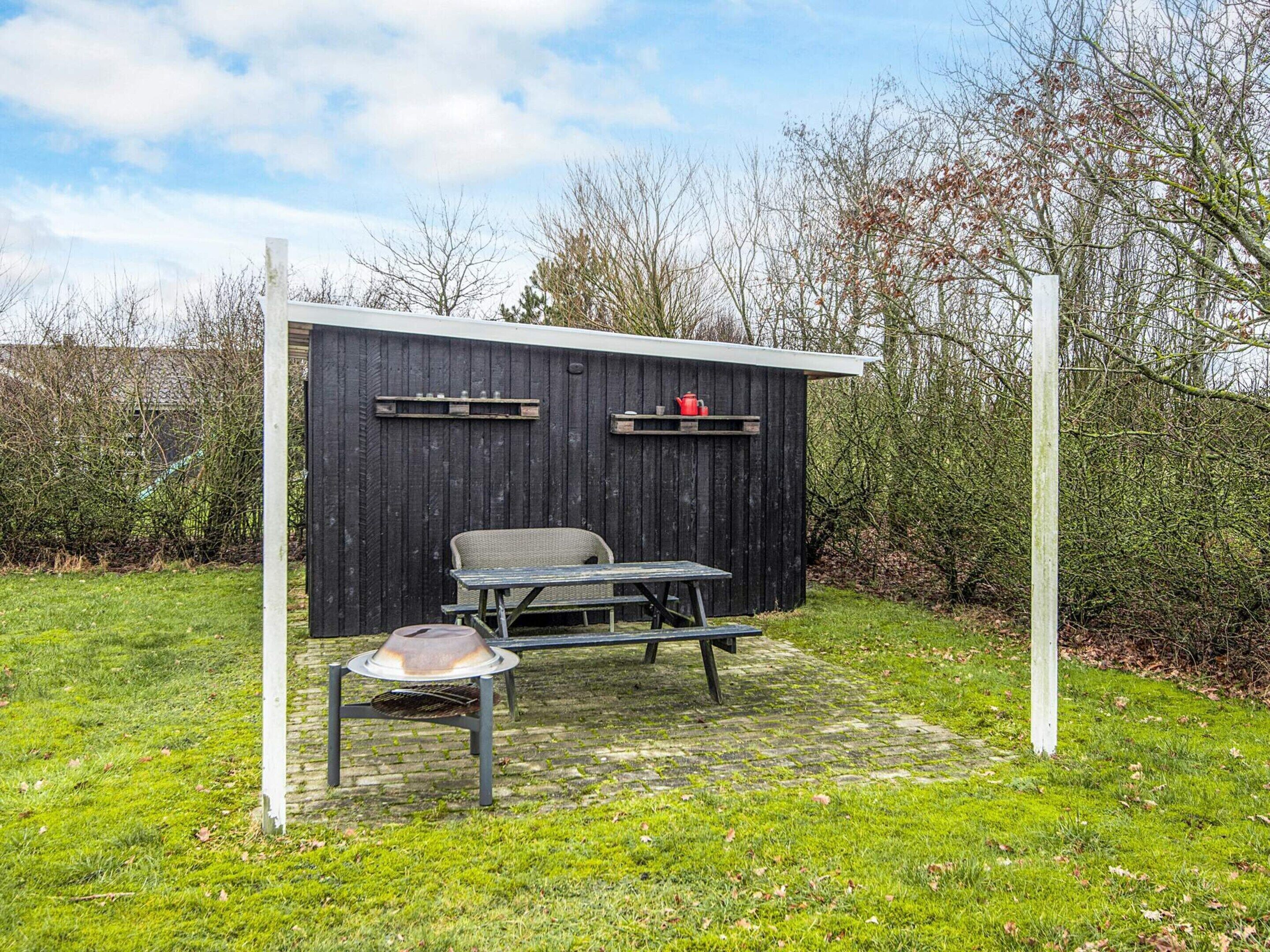 Ein kleiner Außenbereich mit Tisch und Stühlen, einem Grill und einer Holzhütte mit Regalen.