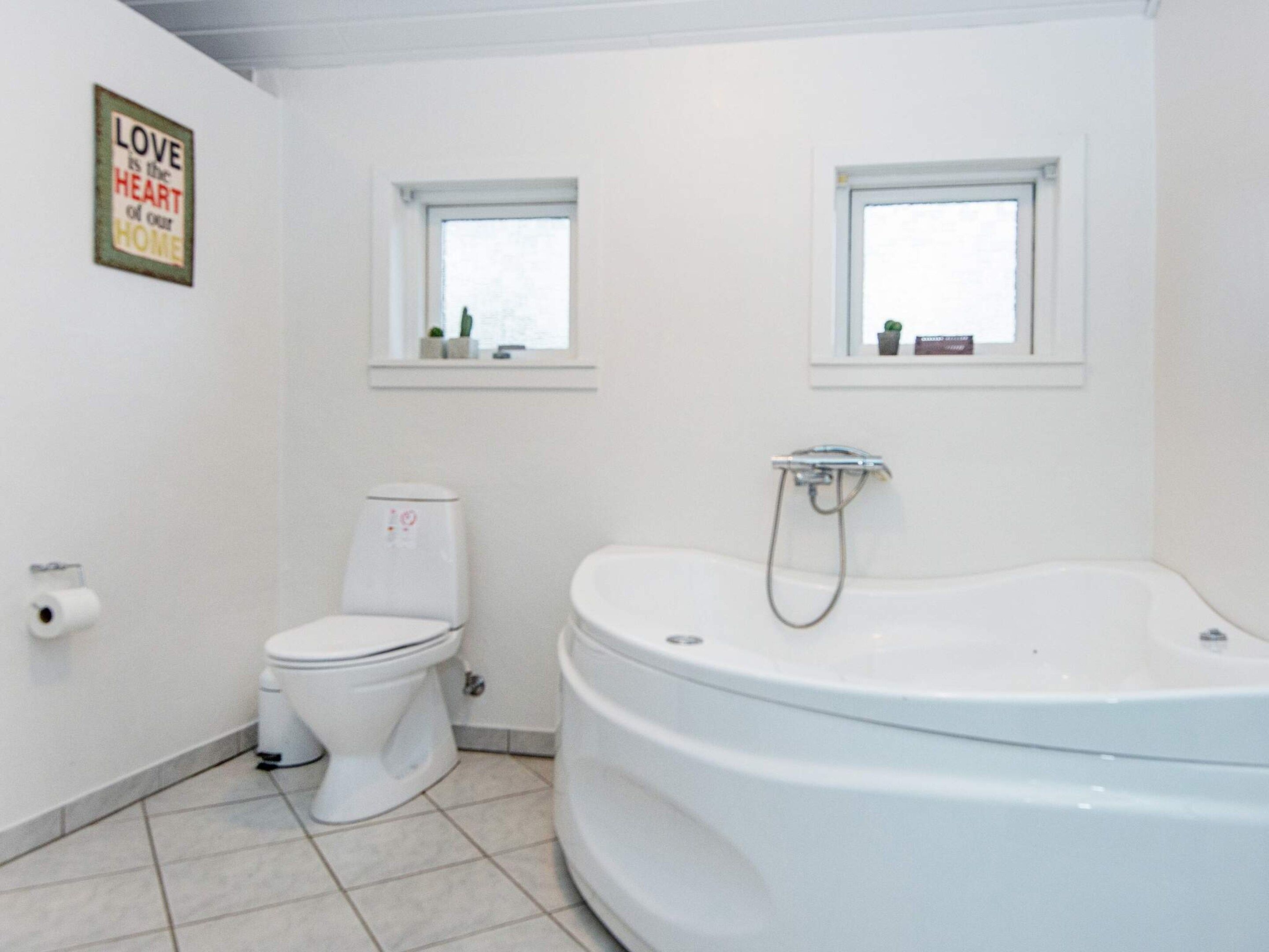 A bathroom with a toilet, a bathtub, and two windows.