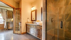Une salle de bain avec une douche en pierre, un meuble-lavabo en bois doté de tiroirs, un miroir et un porte-serviettes.