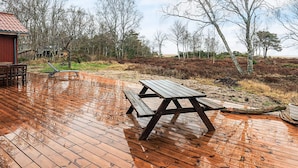 Una terraza de madera con una mesa de picnic y bancos, rodeada de árboles y vistas a la playa.