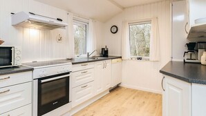 Una cocina moderna con armarios blancos, horno Bosch, microondas, pileta y ventana con cortinas.