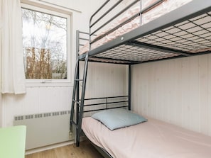 A bunk bed with a ladder, a window with curtains, and a radiator.