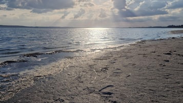 Una playa con huellas en la arena, una masa de agua y una tierra firme distante.