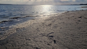 Una playa con huellas, un velero a lo lejos y un cielo nublado.