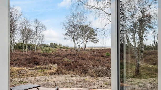 Una terraza de madera con mesa y sillas, con vista a un paisaje natural con árboles y arbustos.