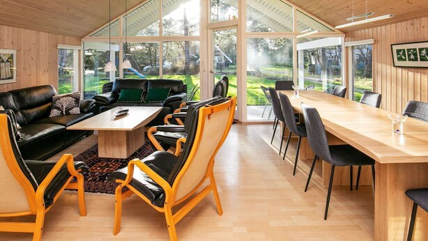 A modern interior with a wooden ceiling, a large glass window, a black leather sofa, a wooden dining table, and a view of a garden. - Spacious Holiday Home in Rødby near Beach (Rodby)
