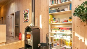A room with a wood-burning stove, a bookshelf with various books and games, a fire extinguisher, and a door leading to another room. - Spacious Holiday Home in Rødby near Beach (Rodby)