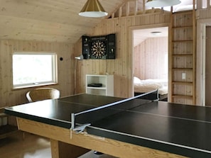 A room with a ping pong table, a dartboard, a bed, and a window.