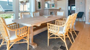 A wooden dining area with a large table and wicker chairs, a kitchen with wooden cabinets, and a view of the outside. - Luxury Retreat With Spa - By Traum Ferienwohnungen (Harboore)