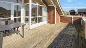 A wooden deck with a table and chairs, large sliding glass doors, and a view of the surrounding area. - Luxury Retreat With Spa - By Traum Ferienwohnungen (Harboore)