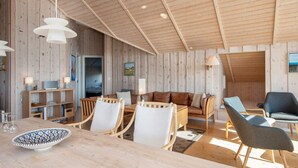 A cozy, wooden-furnished living room with a dining area, a sofa, and a TV. - Luxury Retreat With Spa - By Traum Ferienwohnungen (Harboore)