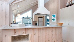 A modern kitchen with wooden paneling, a central island with a bowl, and a view of the outside. - Luxury Retreat With Spa - By Traum Ferienwohnungen (Harboore)