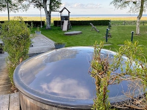 A hot tub with a wooden deck, a swing set, and a view of the beach. - 4 Star Holiday Home in Hadsund (Hadsund)