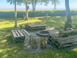 Un espace extérieur aménagé avec des bancs en bois et un foyer, entouré d’arbres et d’un champ d’herbe.