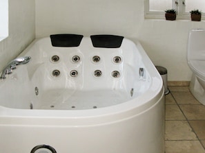 A white bathtub with multiple jets, a handheld showerhead, and a small trash bin.