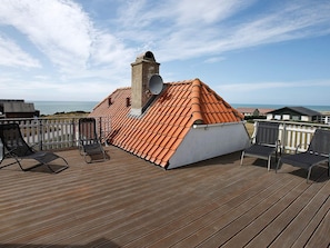 A rooftop terrace with a tiled roof, a chimney, and a view of the sea.