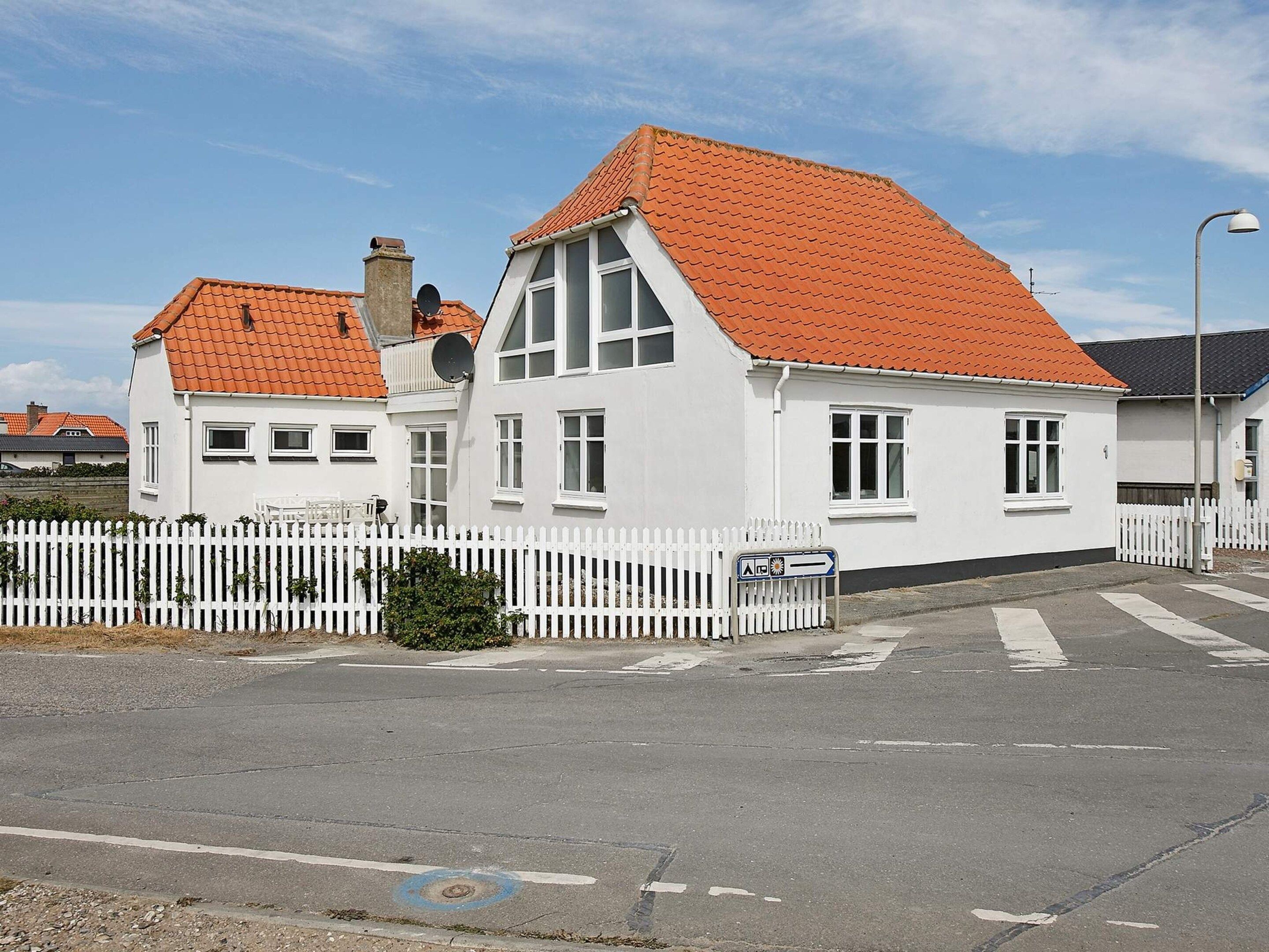 A white building with a red-tiled roof, a white picket fence, and a clear sky.