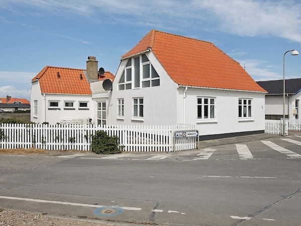 A white building with a red-tiled roof, a white picket fence, and a clear sky.