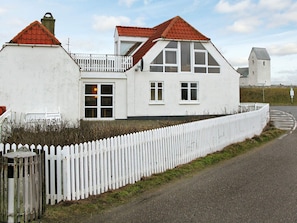 A white building with a red roof, a white picket fence, and a road in front.