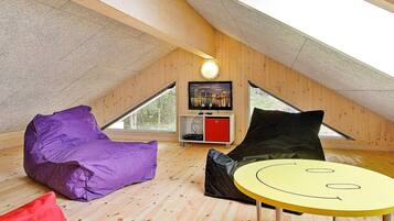 Ein gemütliches Dachzimmer mit schrägem Dach, einem Fernseher auf einem Holzregal und einem großen Fenster.