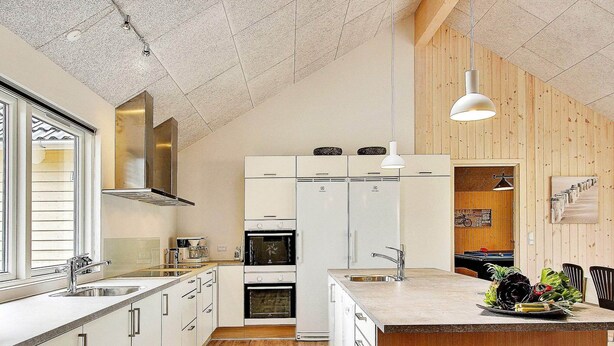 A modern kitchen with white cabinetry, a wooden island, and a dining area with black chairs. - Spacious Holiday Home in Glesborg near Ocean (Glesborg)