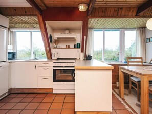 A compact kitchen with white cabinets, a stove, and a sink. There is a window providing natural light and a view of greenery outside.
