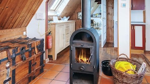 A cozy attic room with a wood-burning stove, wooden furniture, and a view of the kitchen through a skylight. - 4 Person Holiday Home in Romo (Rømø)