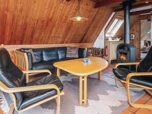 A cozy room with a wooden ceiling, a black leather sofa, a wooden coffee table, and a fireplace.
