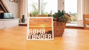 A table with a calendar titled "FERIEGUIDEN 2025 ROMO TÖNDER" and a wicker basket with plants. - 4 Person Holiday Home in Romo (Rømø)