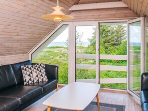 A modern interior with a black leather sofa, a white table, and a large glass door leading to a grassy outdoor area. - 8 Person Holiday Home in Tarm (Tarm)