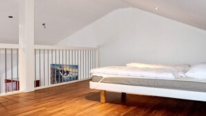 A bedroom with a sloped ceiling, a wooden floor, a bed with white bedding, and a painting on the wall.