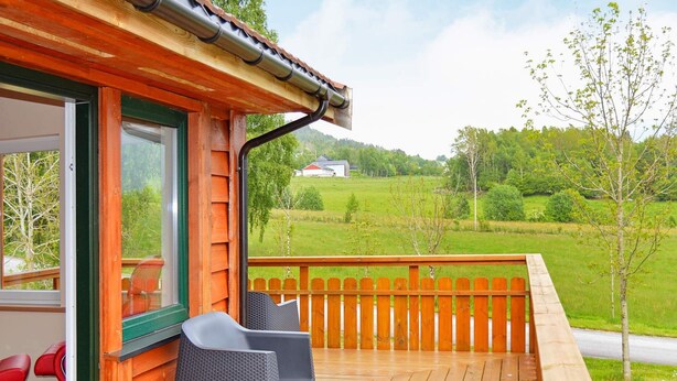 A wooden deck with two wicker chairs, a wooden railing, and a view of a green landscape.