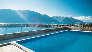 A pool with a wooden deck, surrounded by a stone wall and a railing, overlooking a body of water and mountains. - Holiday Home in Eidsvåg (Molde)