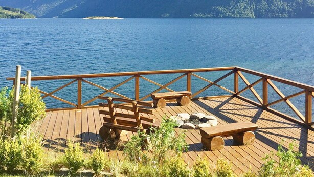 A wooden deck with a railing overlooking a lake, surrounded by greenery and mountains in the background. - Holiday Home in Eidsvåg (Molde)