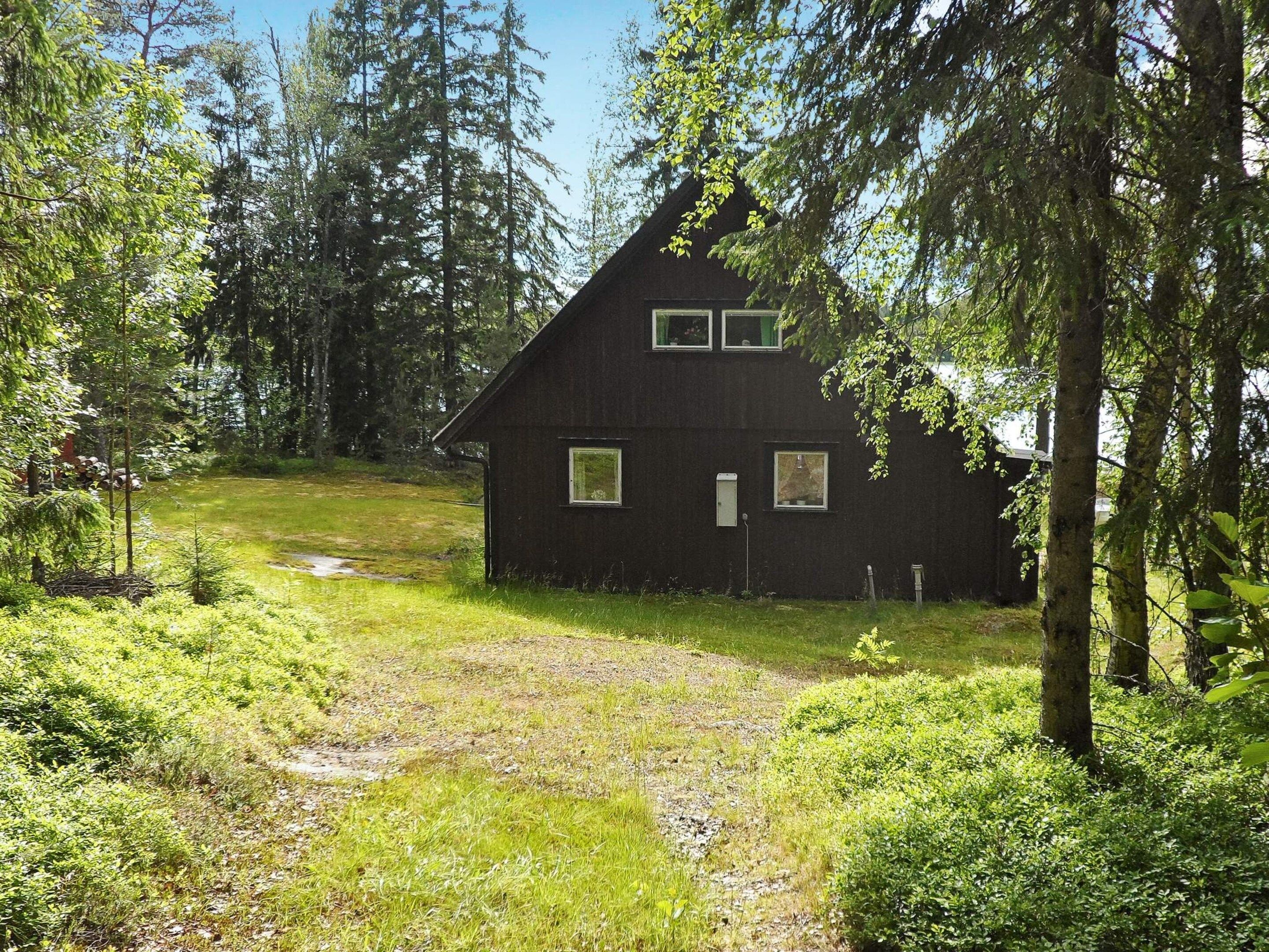 A rustic cabin with a sloped roof, surrounded by dense forest.