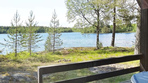A wooden deck with a view of a lake and trees. - 5 Person Holiday Home in Logdea (Lögdeå)