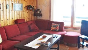 A cozy living room with a red sofa, a wooden coffee table, and a window with a view. - 5 Person Holiday Home in Logdea (Lögdeå)
