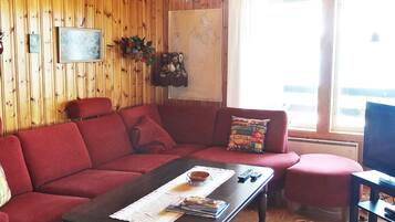 A cozy living room with a red sofa, a wooden coffee table with magazines, and a large window providing natural light.