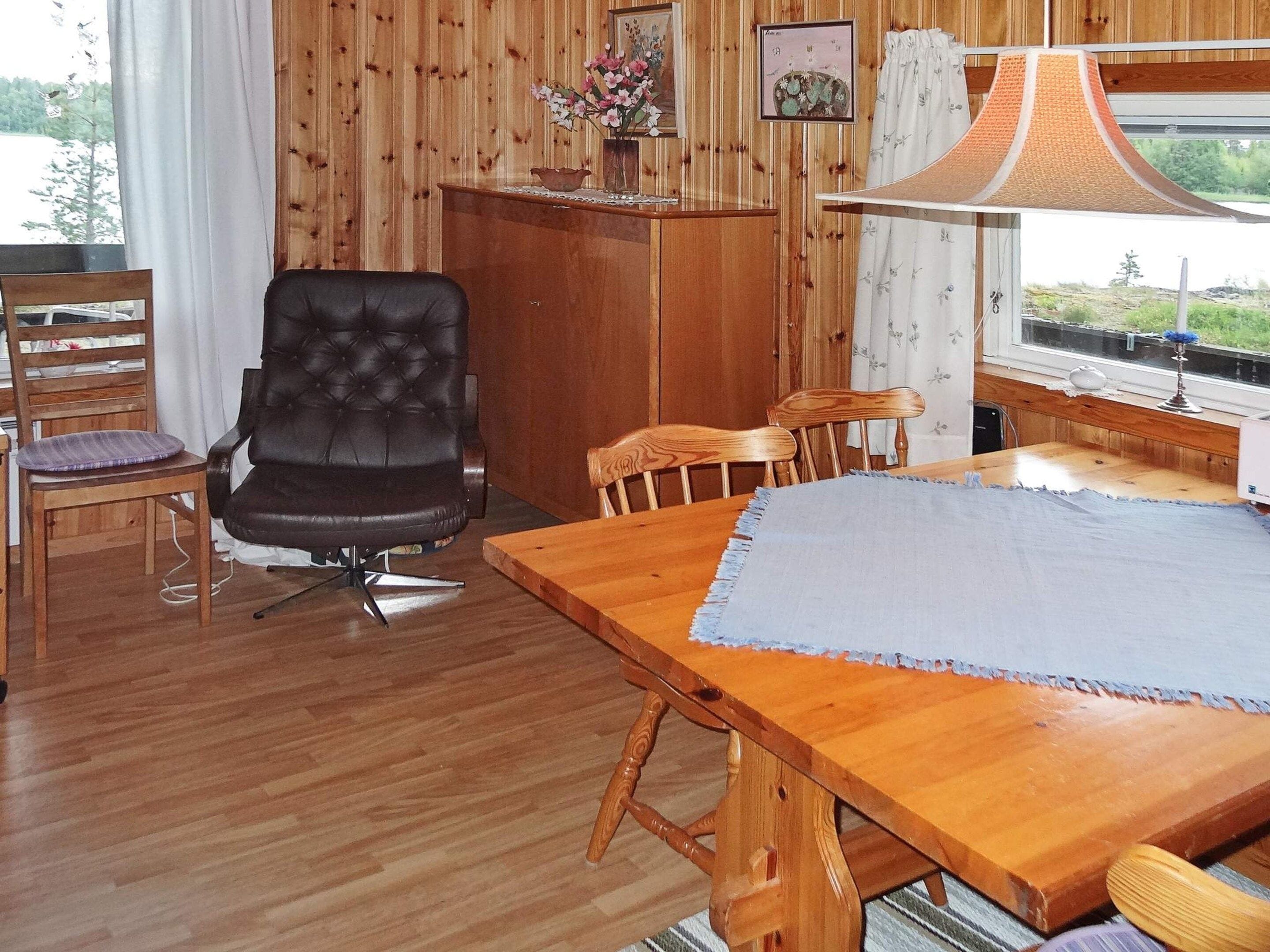 A wooden interior with a dining table, chairs, a black leather chair, a wooden cabinet, and a window with a view.