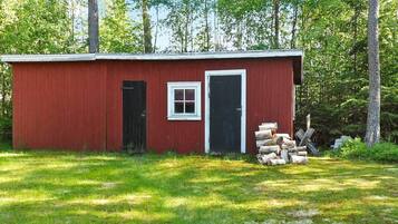 A red wooden shed with a black door and a small window, surrounded by a grassy area and trees.