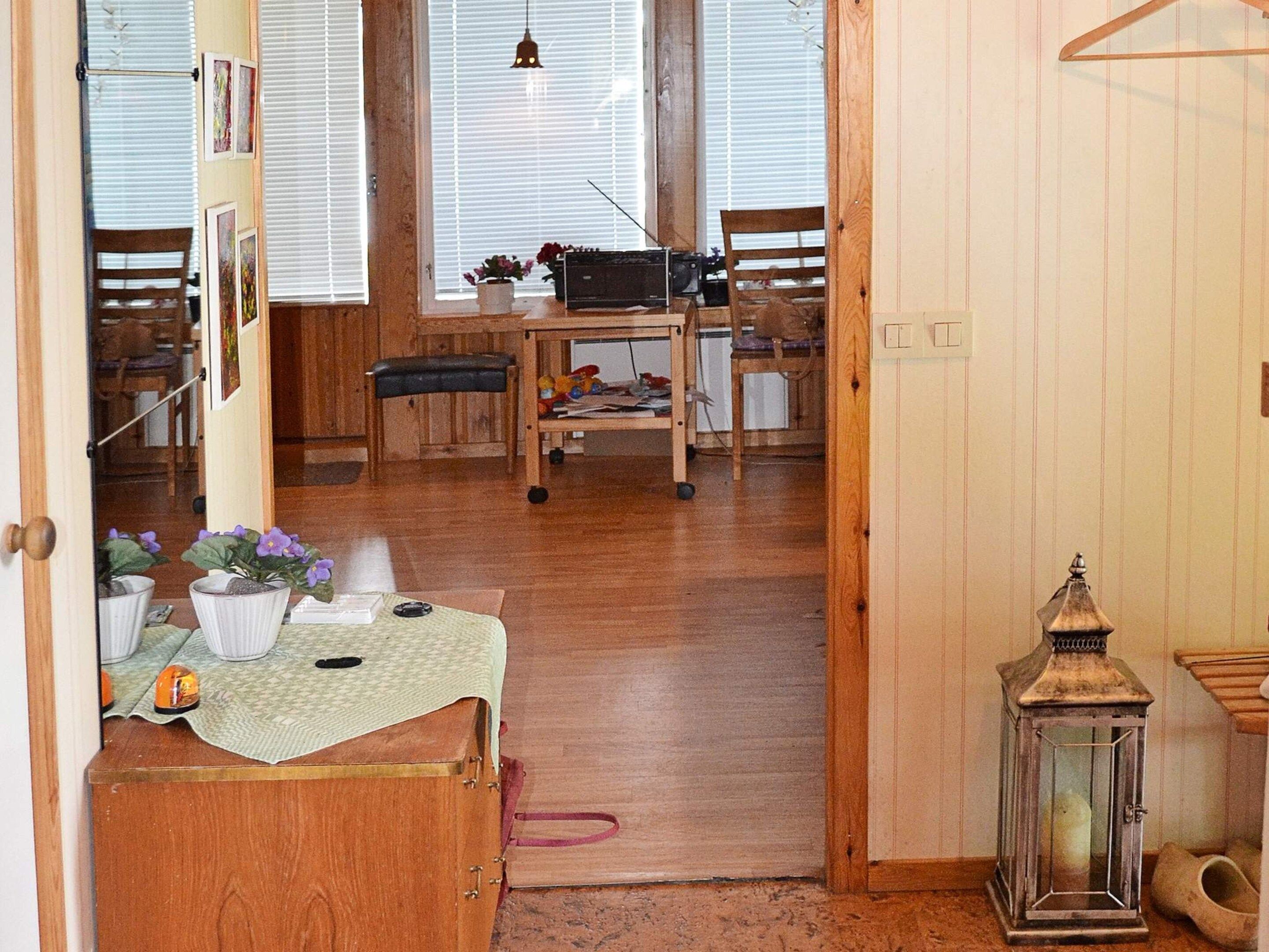 A wooden interior with a dining table, chairs, a bench, a small table with a cloth, and a lantern.