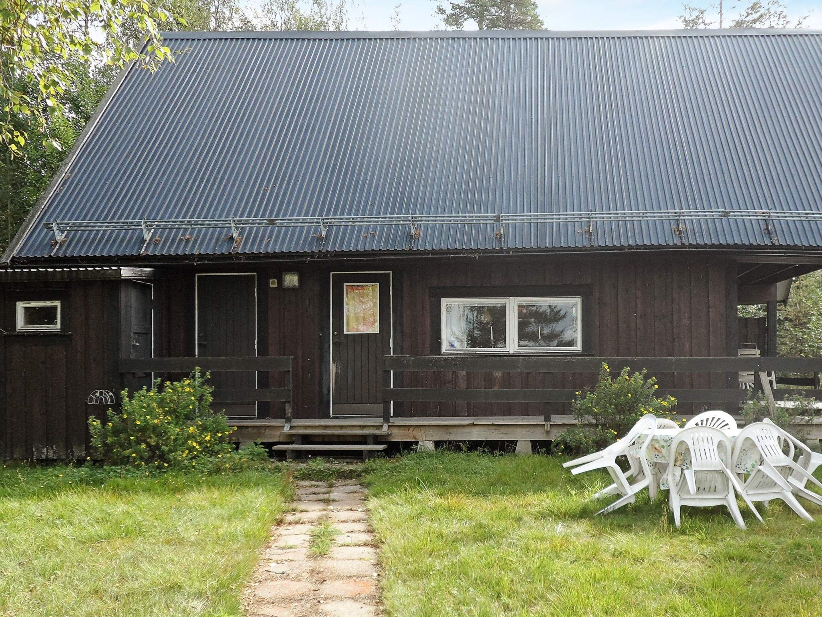 A wooden building with a metal roof, a front door, and a window. There is a stone pathway leading to the entrance.
