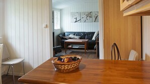 A dining area with a wooden table and a basket of fruit. A black leather sofa and a wooden coffee table are in the background. - Holiday Home in Austrheim (Austrheim)