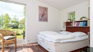 Ein Schlafzimmer mit Bett, Stuhl, Bücherregal und Fenster mit Blick auf Grünflächen.