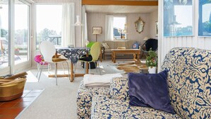 A spacious living room with a large window, a sofa with patterned upholstery, a dining table, and a chair. - 6 Person Holiday Home in Juelsminde (Horsens)