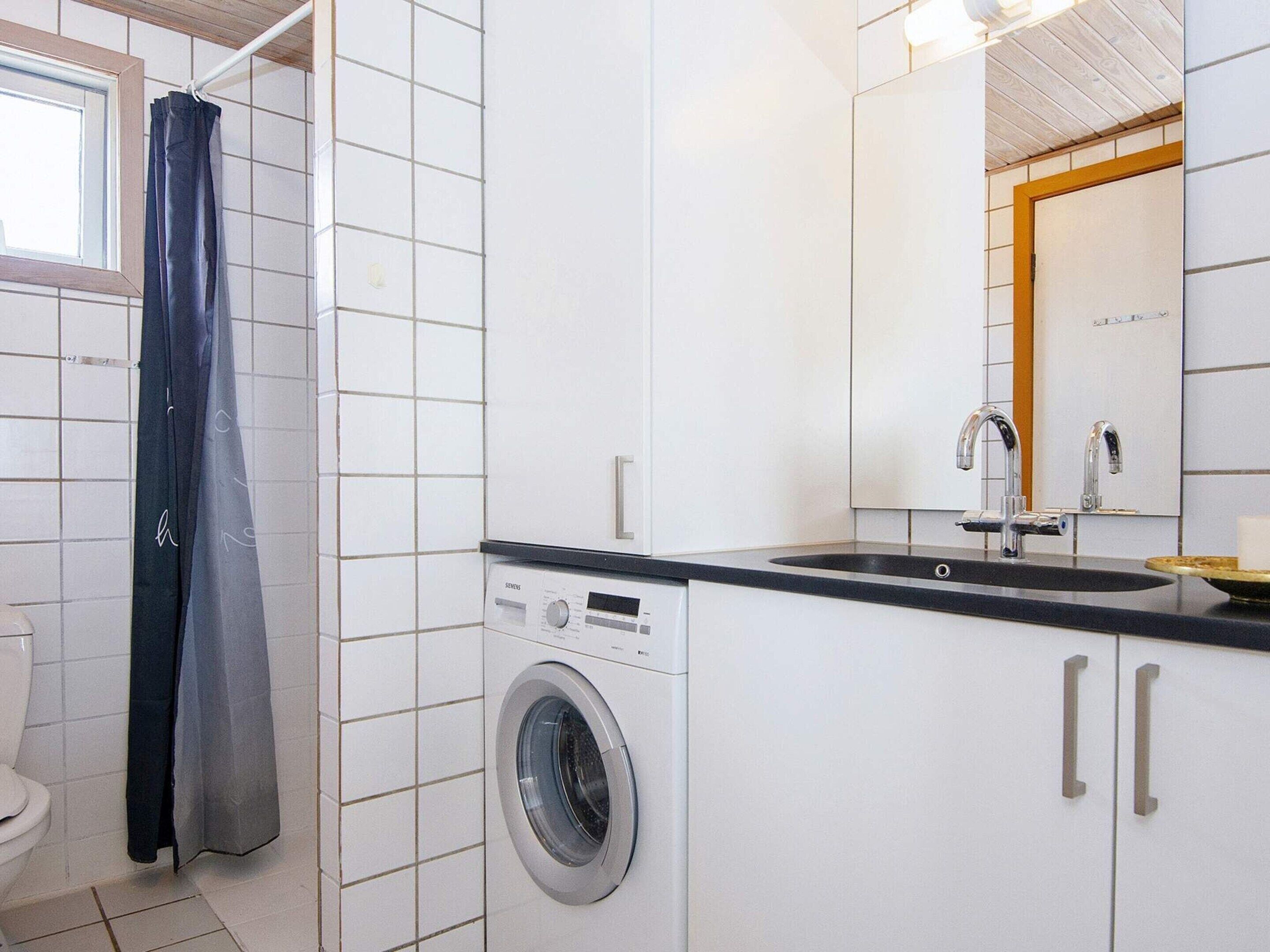 A compact bathroom with a washing machine, a sink, and a mirror.