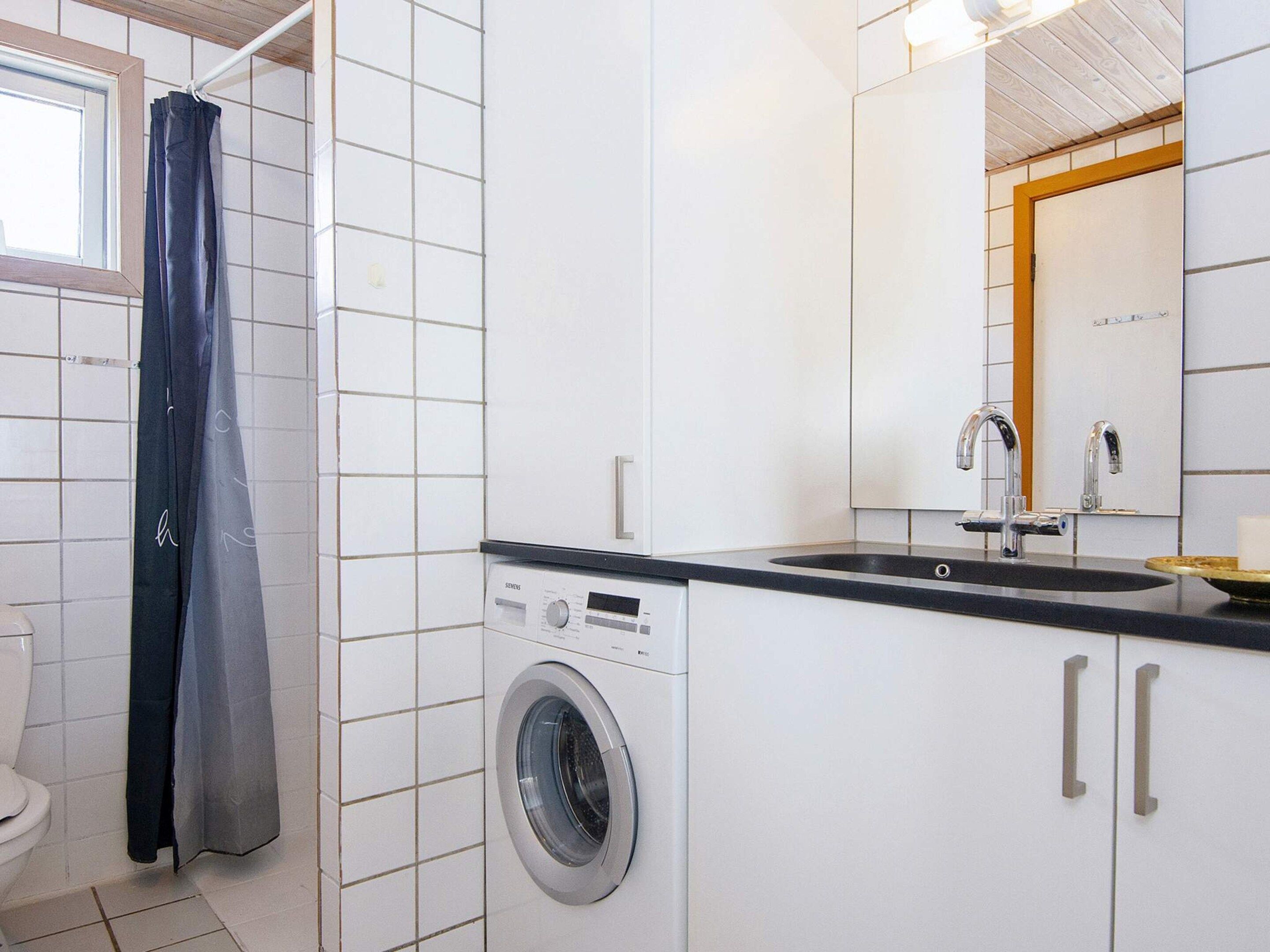 A compact bathroom with a washing machine, a sink, and a shower curtain.