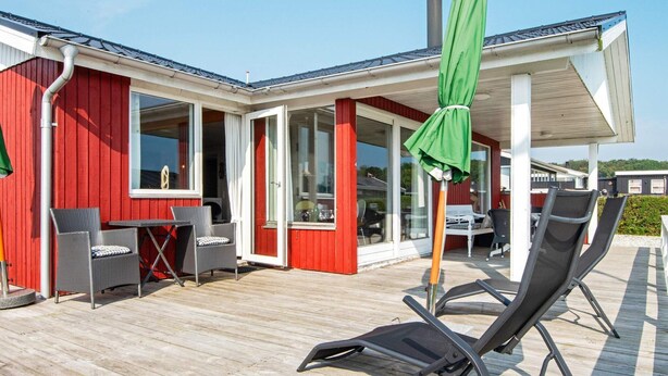 A covered outdoor area with a wooden deck, red walls, and a green umbrella. - 6 Person Holiday Home in Juelsminde (Horsens)